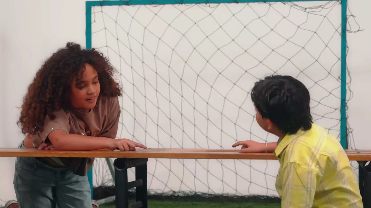 A child sitting at a bench with a goal net behind