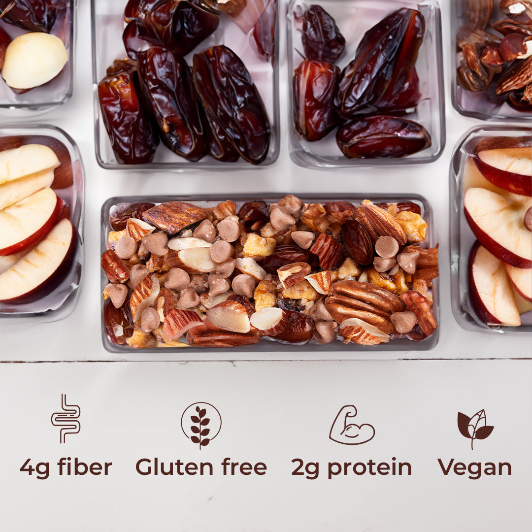 Top View: Unwrapped Apple Pecan Snack bar with sliced apples to its sides, dates at the top of the image on a white wood table on top of 4 icons: 4g Fiber, Gluten free, 2g Protein and Vegan.